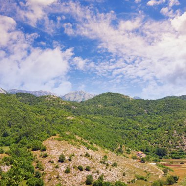 Güneşli yaz gününde güzel dağ manzarası: yeşil dağ sırası, beyaz bulutlar ile pitoresk mavi gökyüzü, vadide küçük bir köy. Balkanlar, Karadağ, Sitnica bölgesi