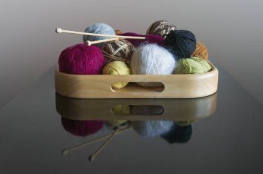 Koyu masa üzerinde ahşap tepside yün ve örgü iğne topları