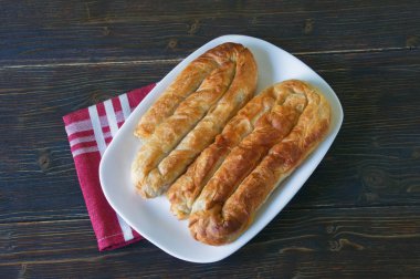 Balkan mutfağı. İki bureks - popüler ulusal yemek - beyaz plaka üzerinde. Düz döşeme, koyu rustik arka plan
