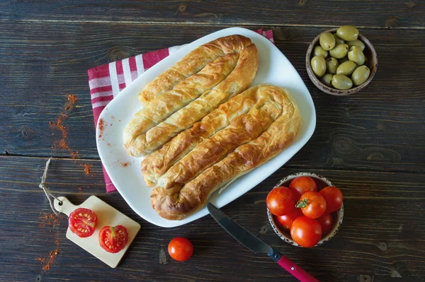 Balkan mutfağı. İki bureks - popüler ulusal yemek - beyaz plaka üzerinde. Düz yatıyordu. Koyu rustik arka plan