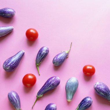 Pembe arka planda mor patlıcanlar ve kırmızı domatesler. Boşluğu kopyala