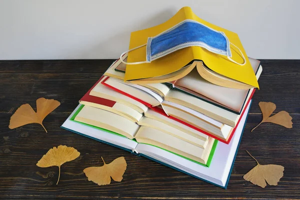 Autumn concept. Books, yellow leaves and face protective mask. Free space for text