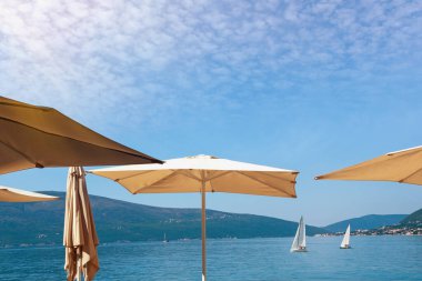 Tatil konsepti. Mavi gökyüzüne karşı güneş şemsiyeleri. Karadağ, Adriyatik Denizi. Tivat kenti yakınlarındaki Kotor Körfezi manzarası