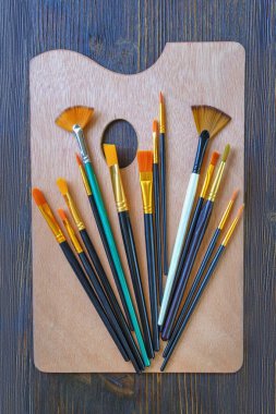 Sanat paleti ve koyu kırsal masa üzerinde çeşitli sanatsal boya fırçaları.