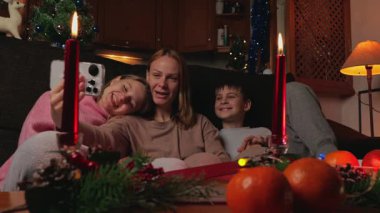 Noel arifesinde evde dört kişilik mutlu bir aile. Anne ve oğlu akıllı telefonlarıyla selfie çekiyorlar.