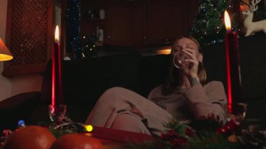 Kanepede oturan genç bir kadın elinde Noel mumuyla oturma odasında kameraya gülümsüyor. Akıllı telefonu olan mutlu bir kadın..