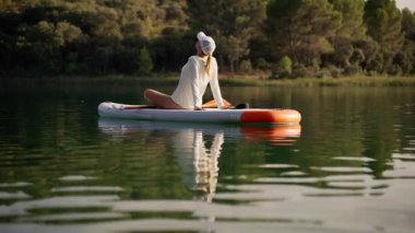 Beyaz mayo ve ceketli kadın nehirde tahta kürek tahtasında oturuyor.