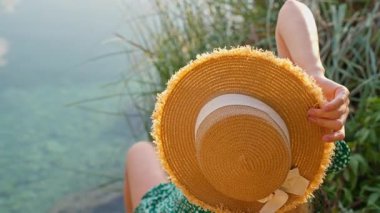 Hasır şapkalı kadın elinde kamış torbasıyla hasır bir şapka tutuyor.