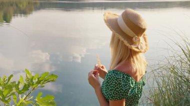 Hasır şapkalı ve güneş gözlüklü kadın göle bakıyor.