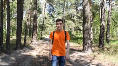 Tişörtlü sırt çantalı genç bir adam ormanda yürüyor.