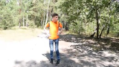 Tişörtlü sırt çantalı genç bir adam ormanda yürüyor.