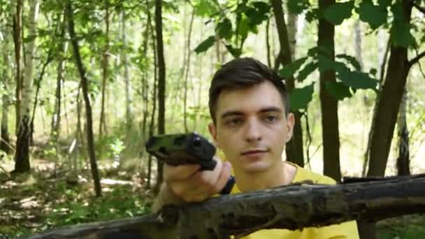 一个穿着黄色T恤的年轻人拿着手枪在森林里射击 — 图库视频影像