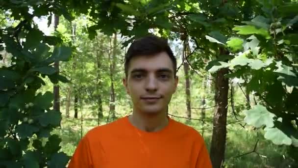 Портрет Молодого Человека Оранжевой Футболке Фоне Зеленой Листвы — стоковое видео