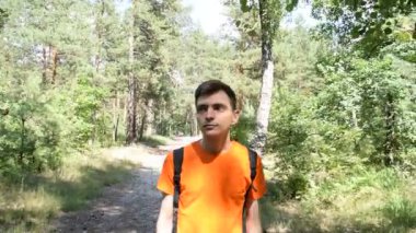 Tişörtlü, sırt çantalı bir gencin portresi ormanda yürür.