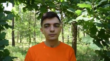 Turuncu tişörtlü genç bir adamın portresi. Ormanda yeşil yapraklı bir arka planda gözlüklü.