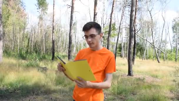 Молодой Парень Оранжевой Футболке Желтой Книгой Фоне Природы — стоковое видео