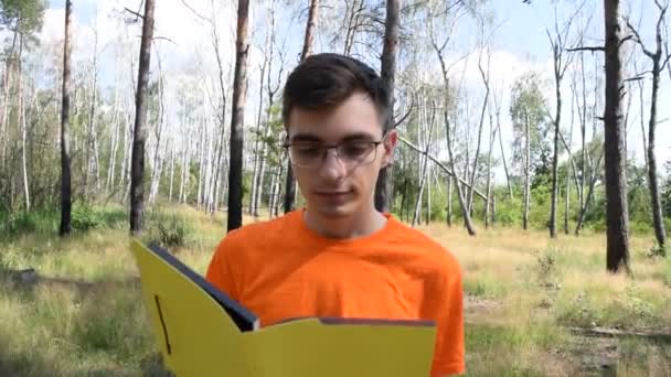 Молодой Парень Оранжевой Футболке Желтой Книгой Фоне Природы — стоковое видео