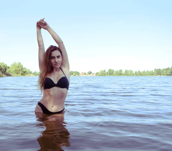 年轻的黑发姑娘穿着黑色泳衣在湖上的水里 — 图库照片