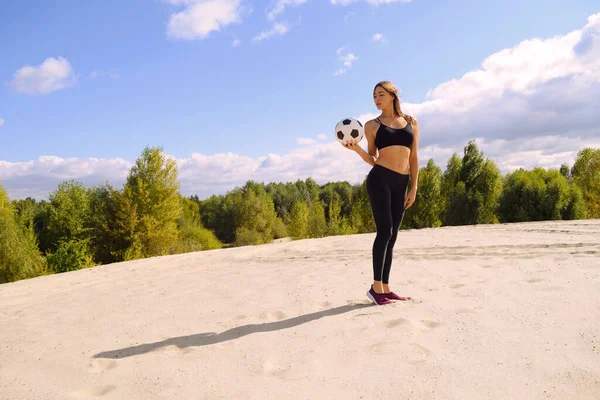 森の近くの砂の上にボールを持った若いスポーツ少女が立っている — ストック写真
