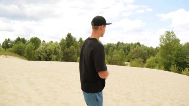 Çölde siyah tişörtlü ve şapkalı genç bir adam.