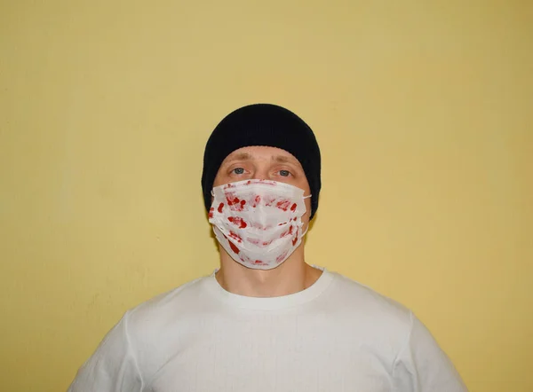 Şapkalı genç bir adam portresi ve duvarda kan lekesi olan tıbbi bir maske.