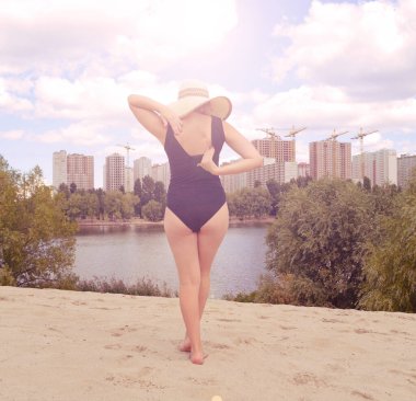 Siyah mayo giymiş şapkalı bir kızın arka görüntüsü. Güneş parlıyor.