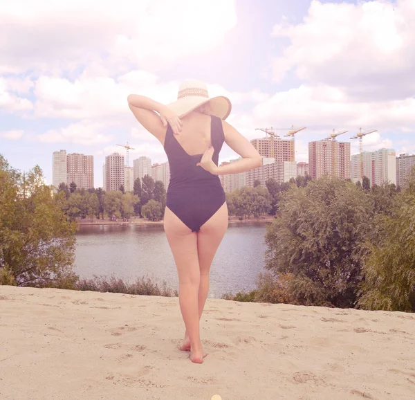 Siyah mayo giymiş şapkalı bir kızın arka görüntüsü. Güneş parlıyor.