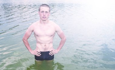 Şortlu genç çıplak adam suyun içinde duruyor.