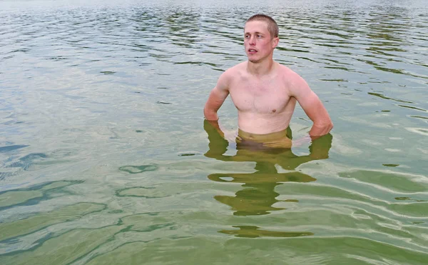 A young naked man stands on a lake in the water. Sports, swimming