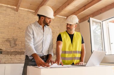 Erkek müteahhit ve mühendis inşaat sırasında dizüstü bilgisayarı kullanarak planı tartışıyor
