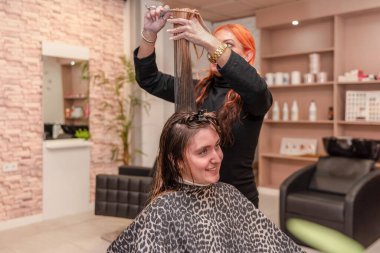 Modern güzellik salonunda gülümseyen müşterinin saçını kesen profesyonel kuaför.