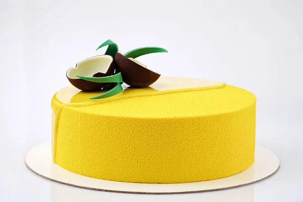 Yellow tropical mousse cake decorated with coconut of chocolate on a white background closeup view