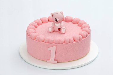 Çocuk pembe mousse kek çikolatalı ayı ve kalp çelenk süslenmiş beyaz bir arka plan üzerinde. Doğum günü pastası bir yaşında.