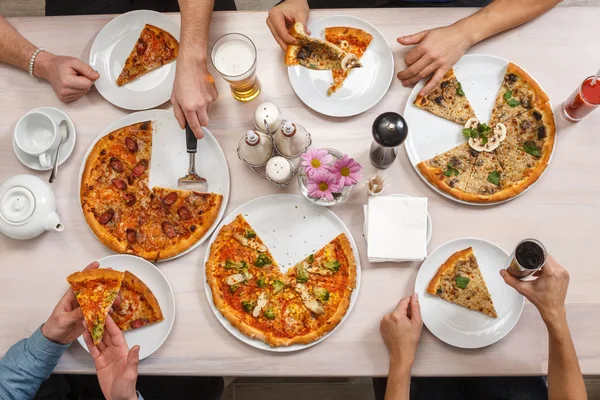 Group of people at the table eating Italian food. Friends eat pizza together. Top view flat lay.