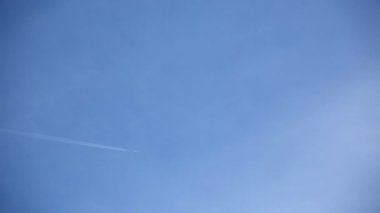 Mavi gökyüzünde beyaz bulutların arasında uçan uçak. Uçakların arkasında kimyasal izler yayılıyor.