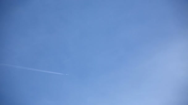 Vliegtuig dat door de witte wolken in de blauwe lucht vliegt. Chemtrails verspreiden zich achter vliegtuigen — Stockvideo