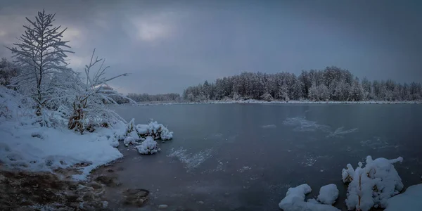 güzel bir akşam kış manzarası. Panoramik bir ısmarlayarak bulutlu havalarda donmuş nehrin karlı kıyıdan