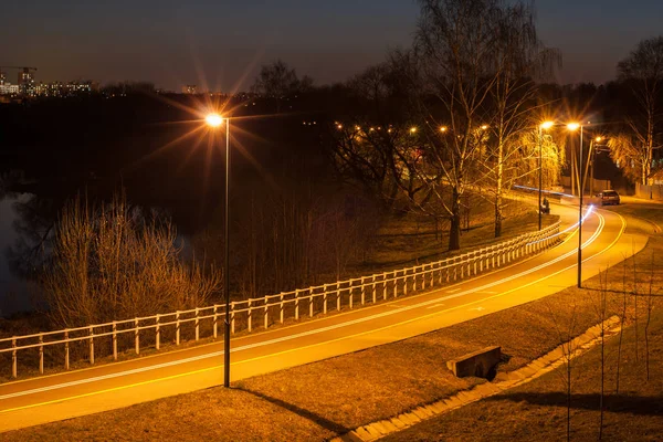 Cycle path on a deserted city outskirts along the river in the late evening. Beautifully Illuminated by street electric lights