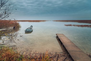 bir gemi, bir eski ahşap iskele ve kıyı sazlık sonbahar alacakaranlık ışığında, bir güzel su yatay için göl kıyısında görüntüleyin
