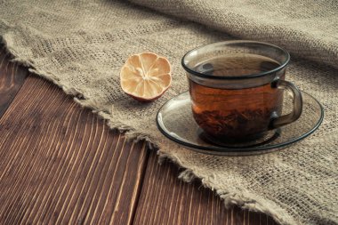 çay şeffaf cam Kupası ve bir kaba çuval bezi masa örtüsü doğal ışık eski kurullarında kenarına kurutulmuş lemon. yan görüş açısı