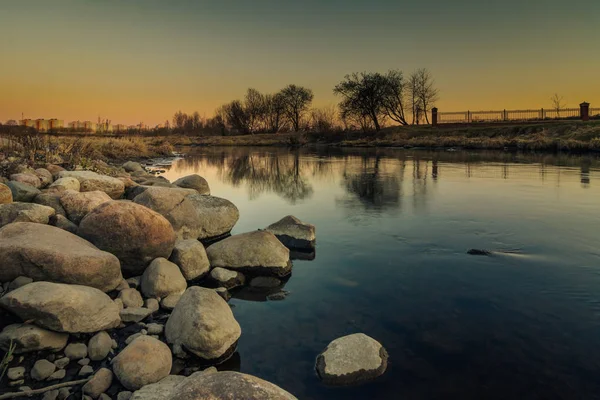 Grote kust stenen op de rivier in de avond stadspark verlicht door schemering licht — Stockfoto