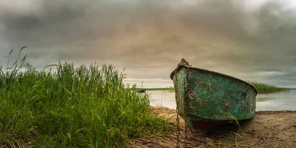 昔のみすぼらしい漁船が湖の上に鎖でつながれていて 葦が輝く劇的な曇りの空に対して 絵に描いたような夏のパノラマ風景 — ストック写真
