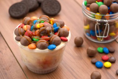 Renkli Doce dondurmayı fincanda konfeti ile kaplıyor ve arkaplanda çikolata düğmelerinin ahşap arka planında izole edilmiş.