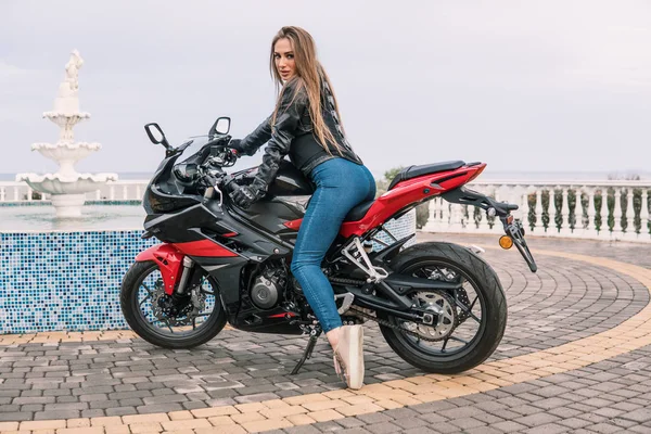 Chica motorista en una chaqueta de cuero en una motocicleta de color negro y rojo —  Fotos de Stock