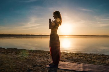 Gün batımında sahilde siluet yoga kadınla.