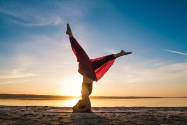 Gün batımında sahilde siluet yoga kadınla.