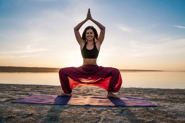 Gün batımında sahilde siluet yoga kadınla.