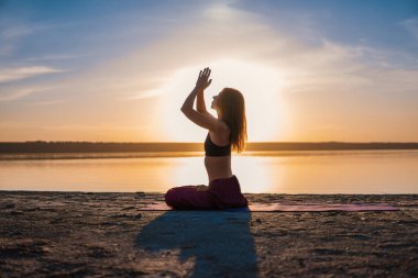 Gün batımında sahilde siluet yoga kadınla.