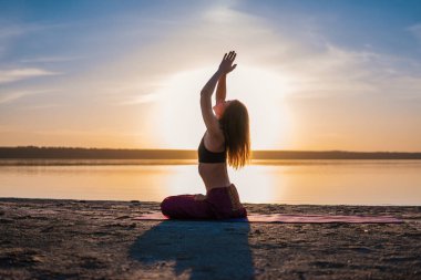 Gün batımında sahilde siluet yoga kadınla.