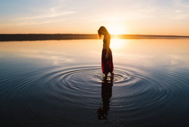 Gün batımında sahilde siluet kadınla. Suda duruyor. Sabah doğal streç ısınma eğitim